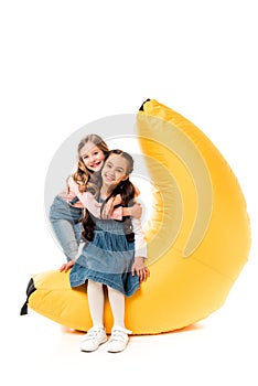 Two smiling kids with bean bag chair on white.