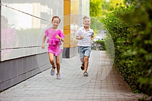 Two smiling kids, boy and girl running together in town, city in summer day