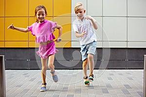 Two smiling kids, boy and girl running together in town, city in summer day