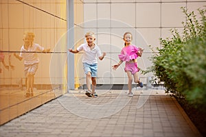 Two smiling kids, boy and girl running together in town, city in summer day