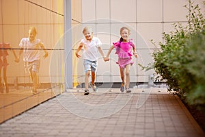 Two smiling kids, boy and girl running together in town, city in summer day