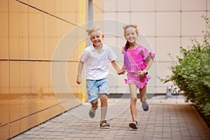 Two smiling kids, boy and girl running together in town, city in summer day