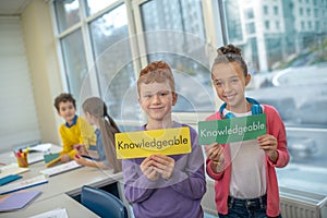 Two smiling kids holding the word knowledgeable