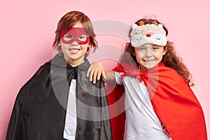 Two smiling kids in superhero suit stand isolated over pink background