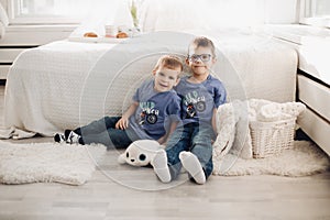 Two smiling male kid posing together at comfortable white bedroom interior