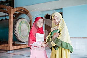 two smiling Muslim girls holding al quran book in their hands