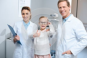 two smiling optometrists and little kid in eyeglasses showing