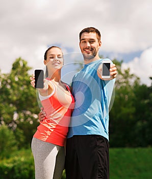 Two smiling people with smartphones outdoors