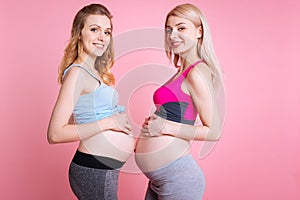 Two smiling pregnancies holding hands on bellies