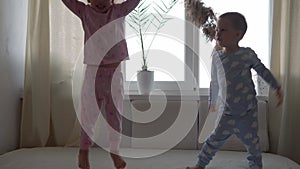Two smiling preshool, toddler children boy and girl lieing on back in pajamas on white bed. Siblings little twins have