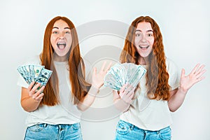 Two smiling redheaded young women both holding cash like playing cards looking happy standing on isolated white backgroung, money