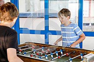 Two smiling school boys playing table soccer. Happy excited children having fun with family game with siblings or