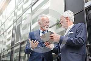 Two smiling senior businessmen working on a tablet and discussing