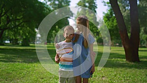 Two smiling siblings posing with rackets. Playful children hugging in park.