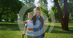 Two smiling siblings posing with rackets. Playful children hugging in park.