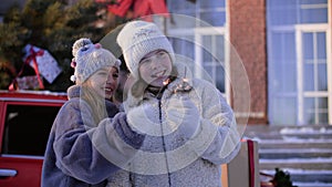Two smiling teen girl holding burning sparklers on winter street on decorative New Year tree background. Happy young