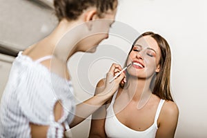 Two smiling teenage girls applying make up at home