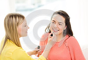 Two smiling teenage girls applying make up at home