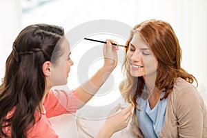 Two smiling teenage girls applying make up at home