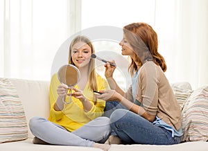 Two smiling teenage girls applying make up at home