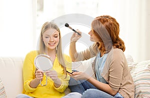 Two smiling teenage girls applying make up at home