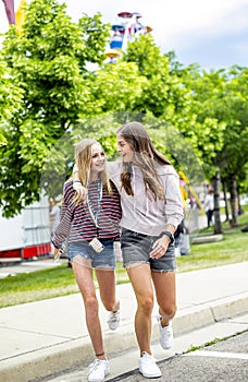 Two smiling teenage girls walking together at an outdoor carnival.