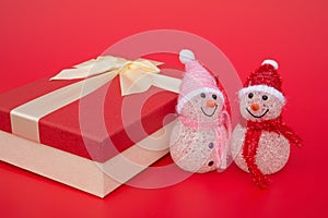 Two smiling toy christmas snowman and a present box on red