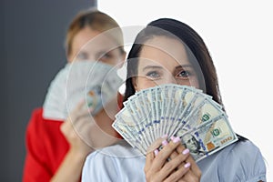 Two smiling women covering face with fan of one hundred dollar bills.