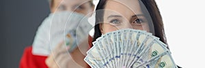 Two smiling women covering face with fan of one hundred dollar bills.