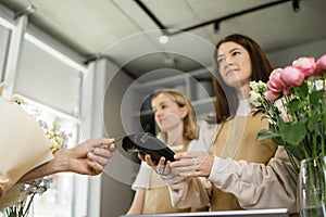 Two woman florists holding card reader machine at counter with customer paying with credit card