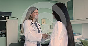 Two smiling women general practitioners in white coats shaking hands