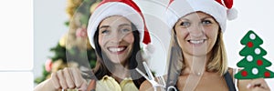 Two smiling women hairdressers in uniforms and santa claus hats hold alarm clock scissors with comb.