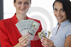 Two smiling women are holding fan of one hundred American dollar bills and credit bank cards.