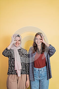two smiling women with ok approval hand gesture affixed to one eye with copyspace above