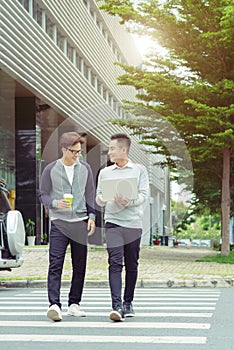 Two smiling young businessmen walking and talking in the city