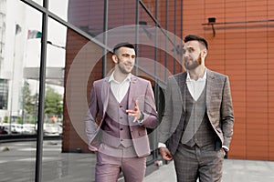 Two smiling young businessmen walking and talking in the city