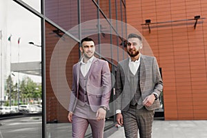 Two smiling young businessmen walking and talking in the city