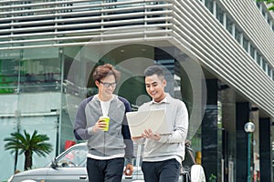 Two smiling young businessmen walking and talking in the city