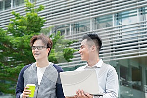 Two smiling young businessmen walking and talking in the city.