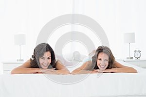 Two smiling young female friends lying in bed