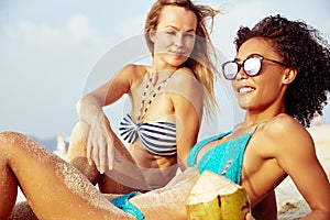 Two smiling young female friends suntanning together on a beach