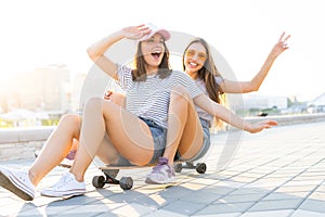 Two smiling young girls having fun while riding on a skateboard at the park.