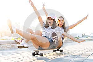 Two smiling young girls having fun while riding on a skateboard at the park.