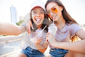 Two smiling young girls having fun while sitting on a skateboard and taking a selfie at the park.