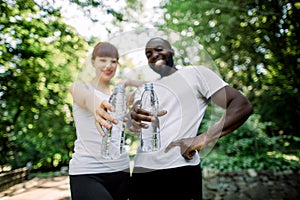 Two smiling young multiracial friends, African man and Caucasian woman, posing to camera after jogging workout outdoors