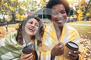 Young women friends chatting outdoors and drinking coffee while enjoying the walk in the park together