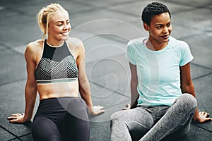 Two smiling young women relaxing together on a gym floor