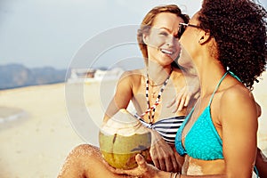 Two smiling young women relaxing together on a tropical beach