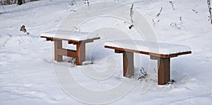Two snow-covered benches in a winter park. The concept of winter loneliness