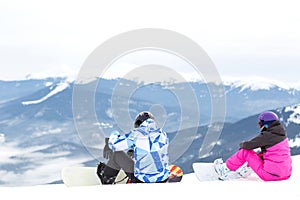 Two snowboarders are sitting on a high mountain slope